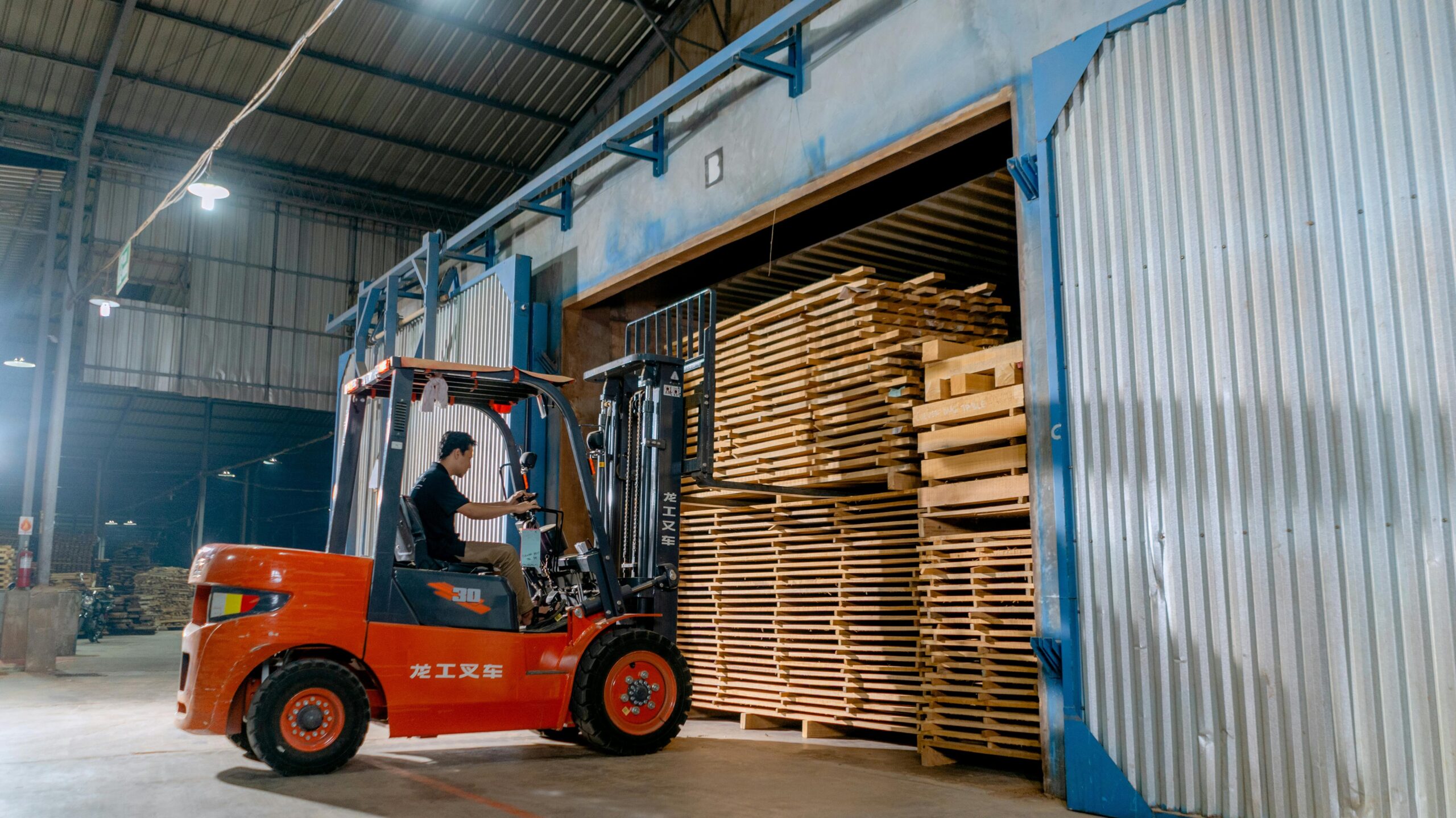 Man operating a forklift indoors loading wooden pallets in a warehouse.